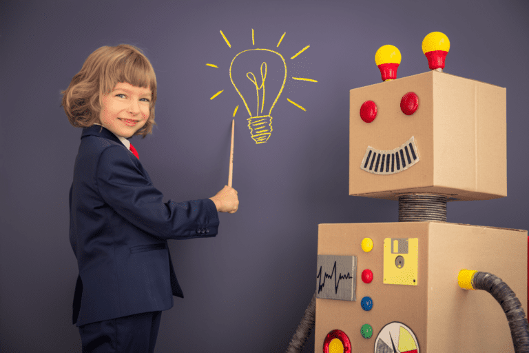 Young boy pointing to a blackboard next to a robot he has built.